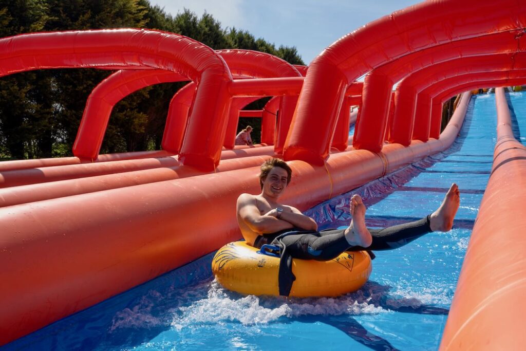 man riding cornwall slip and slide 360ft inflatable tube slide splashing water outdoor newquay