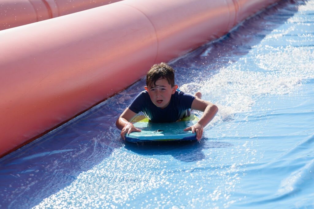Boy bodyboarding down the giant inflatable slide at Cornwall Slip and Slide, Atlantic Reach Resort near Newquay